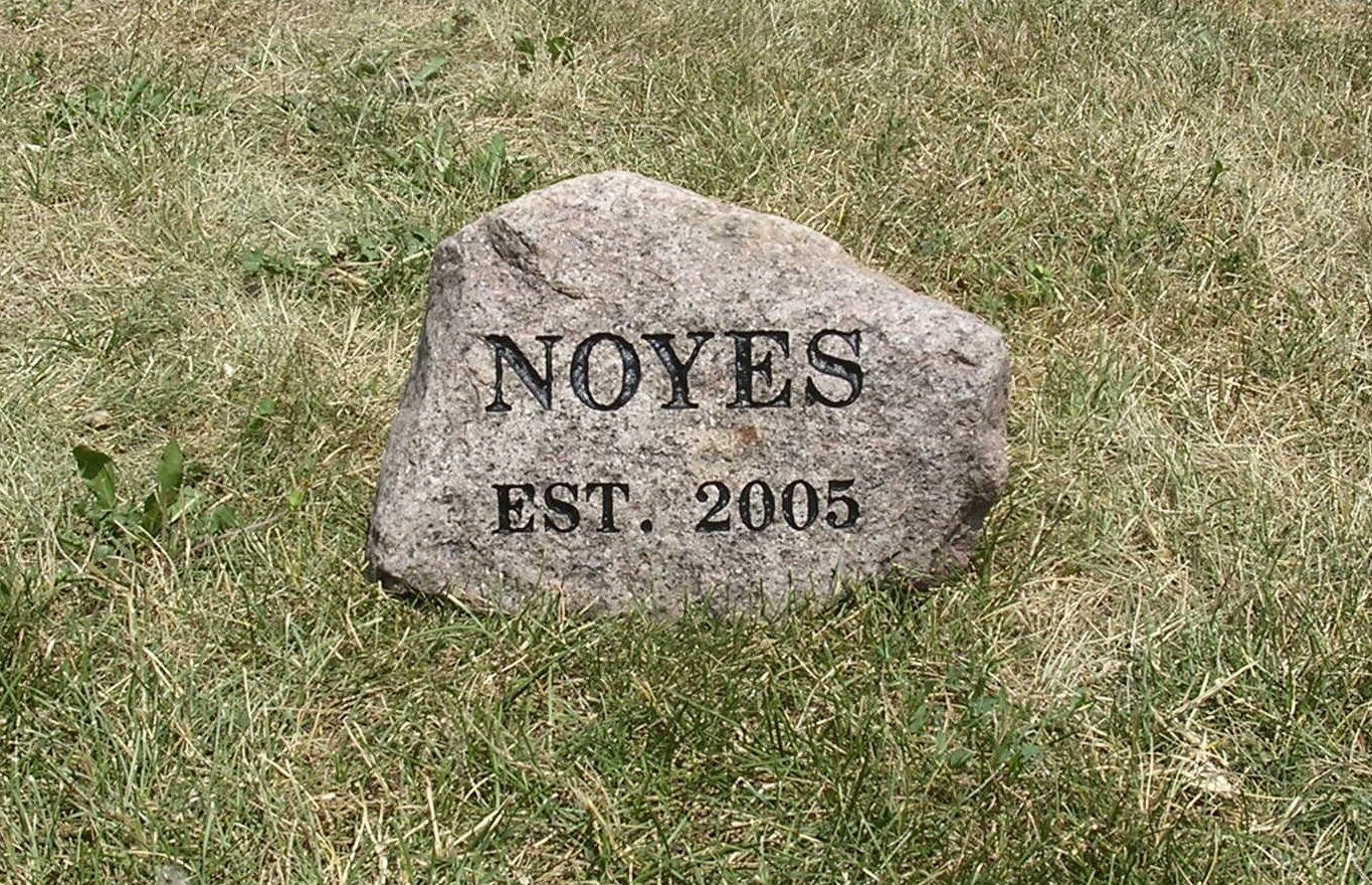 A stone marker on grass engraved with “NOYES EST. 2005.”.