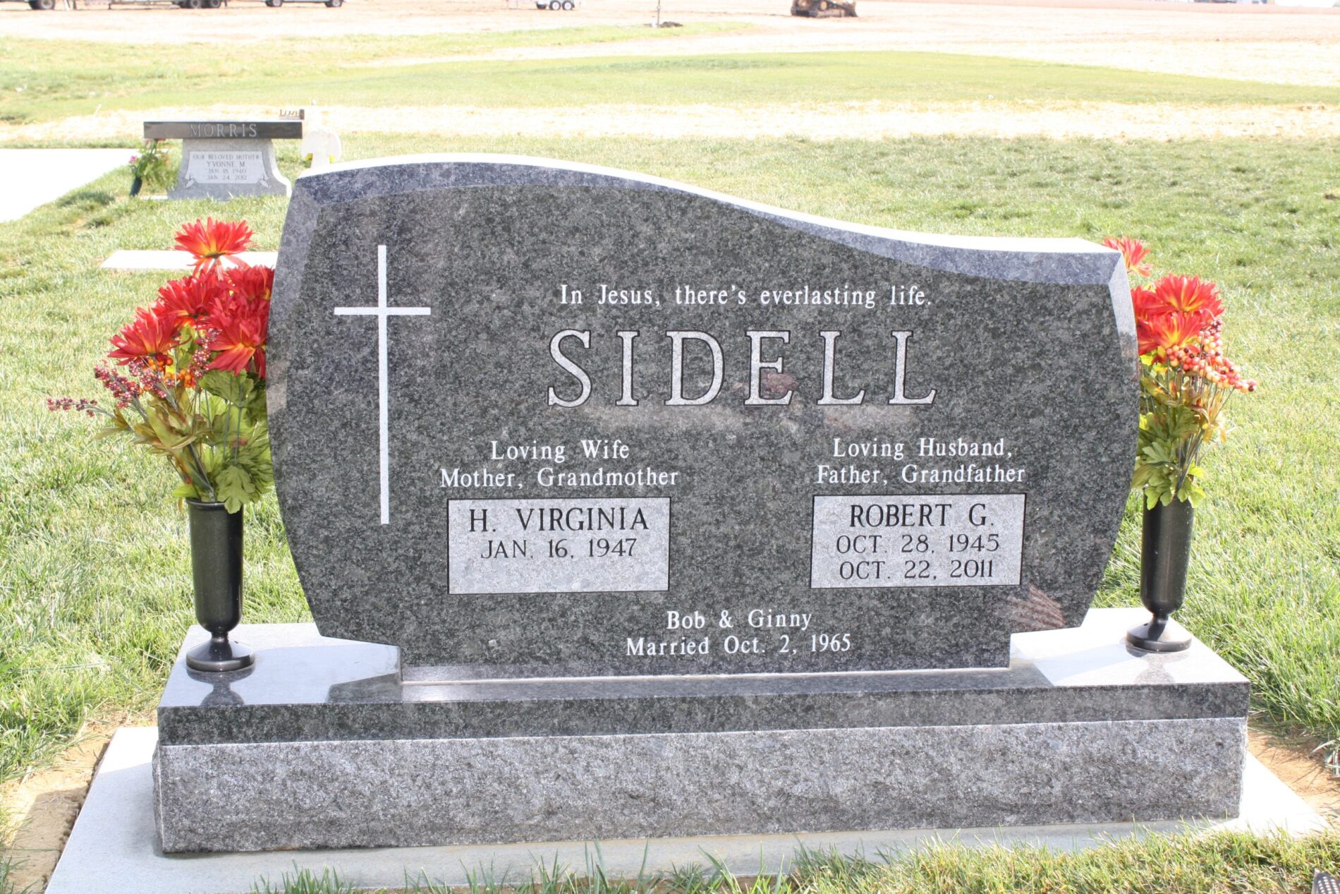 Gray headstone for H. Virginia and Robert G. Sidell with flowers, engraved with dates, names, and an inscription.