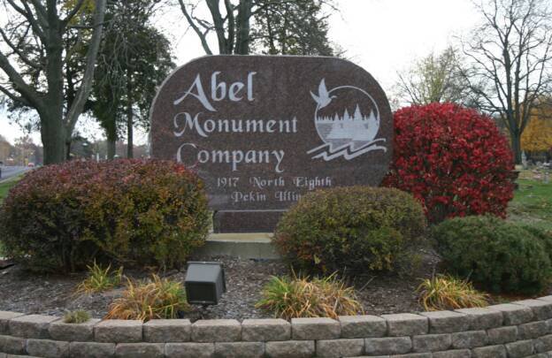 Large stone sign for Abel Monument Company, 1912 North Eighth, Pekin, Illinois, surrounded by shrubs and landscaping.