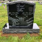 Polished granite upright headstone monument with engraved design in a cemetery memorial setting.